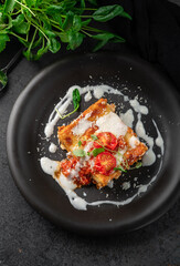 A portion of meat lasagna with bolognese sauce and mozzarella cheese on a black plate, top view