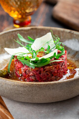 Beef tartare with dried tomatoes decorated with parmesan and arugula is served in a plate on a wooden table, close up