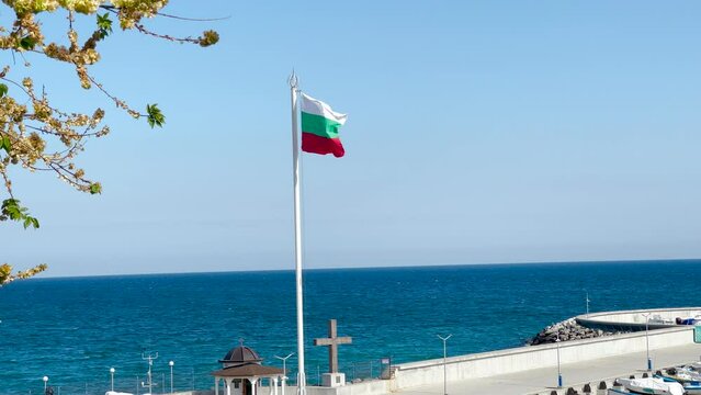 The flag of Bulgaria flutters in the wind on the seashore. Bulgarian flag on the pier on a sunny summer day.