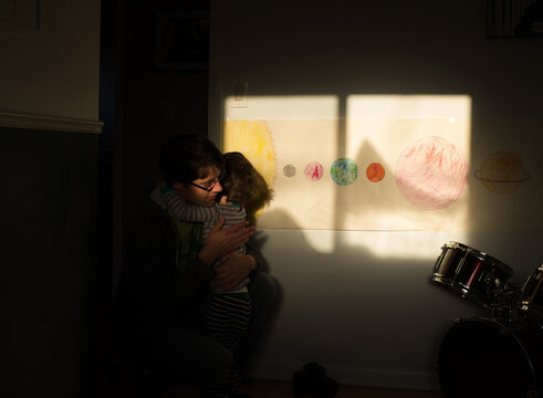 boy hugs dad in sunlight inside with planet drawings behind him