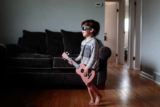 little boy play ukulele in home with sunglasses