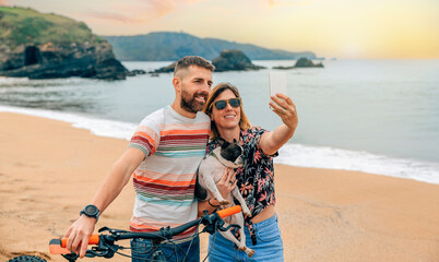 Young couple with their dog taking a selfie on the beach - Powered by Adobe