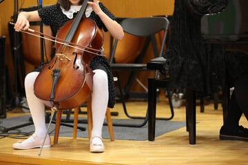 Girl student plays the cello with a bow sitting on a chair at a music lesson at school