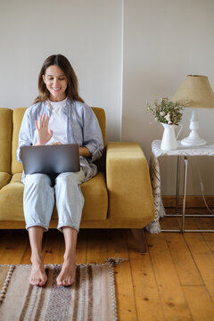 Woman with laptop sitting on the sofa at home starting online meeting