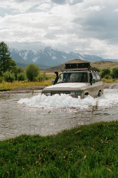 SUV crosses the river with mountains  in the background