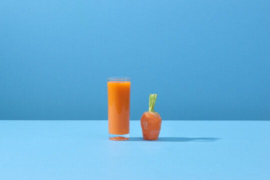 Carrot and glass of fresh juice on blue background