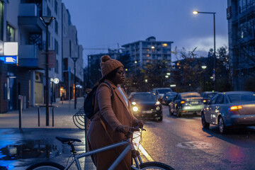 woman with bicycle crossing the road by night, city lights