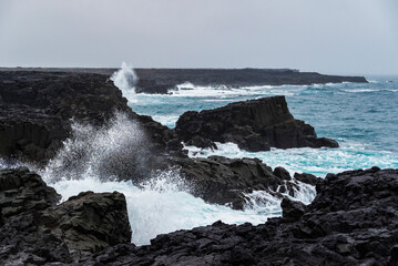 The coastal cliffs near Brimketill rock pool on a stormy day, with huge sea waves crashing against...