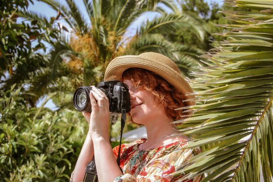 red-haired woman in straw hat takes pictures