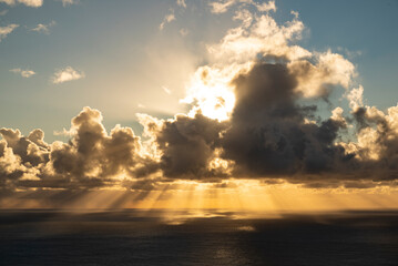 Beautiful cloudscape over the Atlantic Ocean on the coast of Madeira at sunset. Warm yellow sun rays penetrate the clouds and shine on the dark water surface.