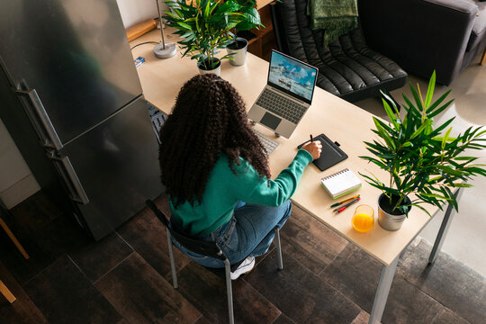 Black woman using graphic table and laptop at home 