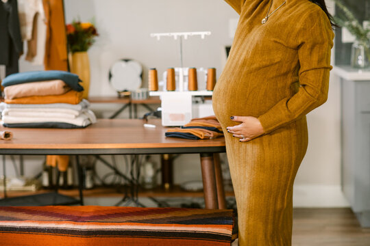 Pregnant touching her belly in sewing atelier