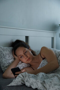 Woman lying in bed and using smartphone after awake