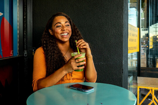 Woman Smiles Holding Green Juice at Cafe