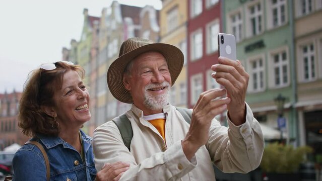 Happy senior couple tourists taking selfie outdoors in historic town