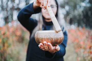 Black dressed buddhist woman holding and playing a tibetan singing bowl with a wooden stock....
