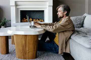 Adult man working on online project on laptop in living room