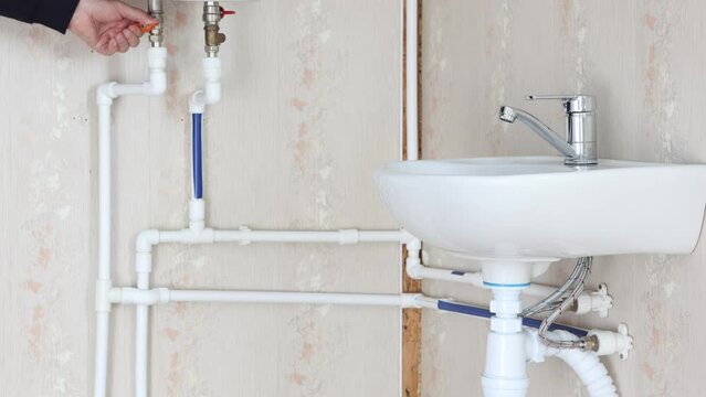 Hand turns water valve in domestic piping system.