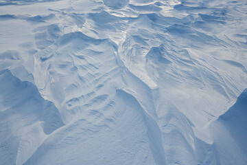 Beautiful winter background with snowy ground. Natural snow texture. Wind sculpted patterns on snow surface. Arctic, Polar region.