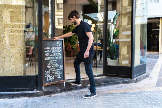 Smiling worker putting stand board near cafe entrance