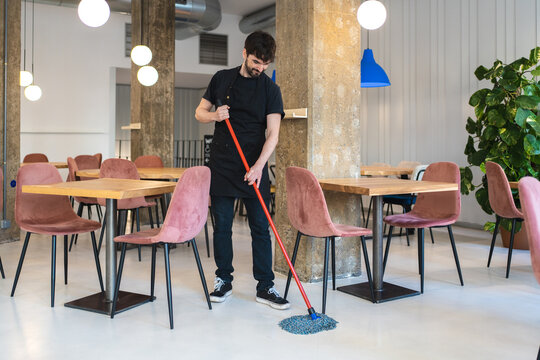 Young man cleaning floor in cafe before opening