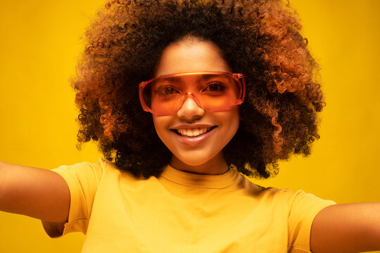 Happy confident young black woman wearing orange sunglasses takes selfie for photo or video blog.