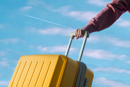 Fototapeta Person holds a travel yellow plastic suitcase