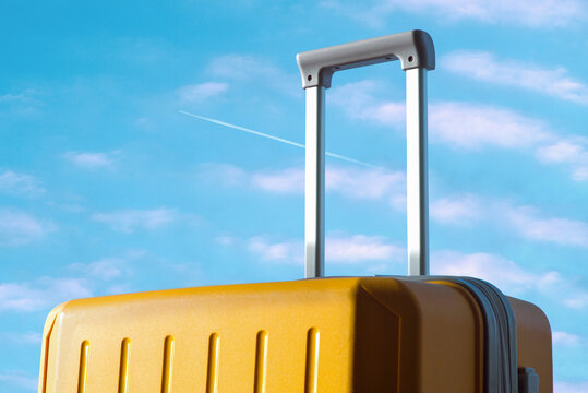 Yellow travel suitcase against a blue sky with an airplane trail