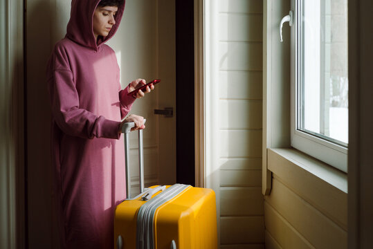 A young woman with a yellow plastic suitcase uses a smartphone 