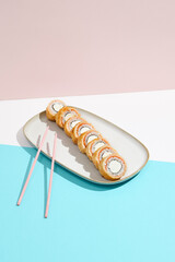 Baked Philadelphia Maki with salmon on ceramic plate. Hot tempura sushi with salmon and philadelphia cheese on coloured background. Japanese menu concept. Hot maki sushi in modern style.