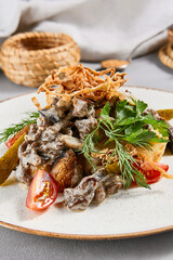Traditional russian food - beef stroganoff with mashed potatoes and creamy gravy. Beef stroganoff with crispy onion on ceramic plate. Meat ragout with mashed, mushrooms and greens on stone background.