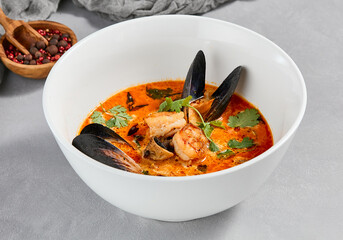 Traditional asian food - tom yam kung with prawn and mussels. Tom yum soup with seafood and coconut milk. Tom yam in ceramic bowl on gray stone background. Oriental cuisine. Asian menu.