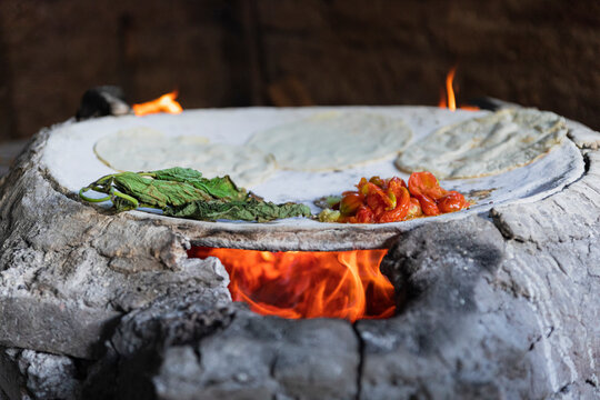 Herbs, tomatoes, and tortillas on a comal with fire inside