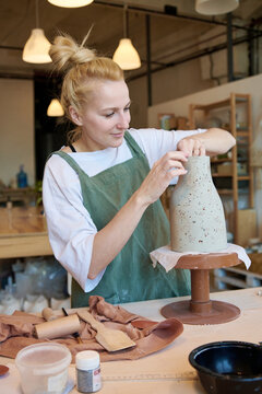 A female potter refines her vase,