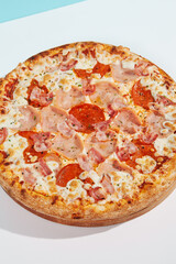 Italian pizza with ham and bacon on coloured background. Meat pizza with bacon and ham in minimal style on blue and orange color. American pizza delivery concept with color backdrop