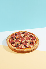 Italian pizza with chicken, salami and sausage on coloured background. Meat pizza with chicken and salami in minimal style on blue color. American pizza delivery concept with color backdrop.