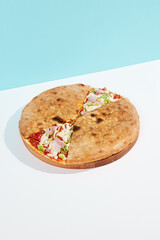 Italian closed pizza with cheese, bacon, tomato on coloured background. Calzone pizza with meat, cheese and vegetables in minimal style. American pizza delivery concept with color backdrop.