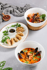 Set of asian food. Pan asian cuisine - Fried udon with beef, tom yam soup, gyoza. Asian food menu. Aesthetic composition with panasian dishes on concrete background.