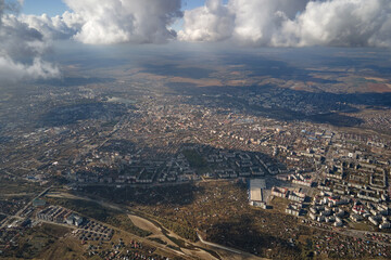 Aerial view from airplane window at high altitude of distant city covered with puffy cumulus clouds...