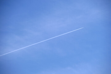 Distant passenger jet plane flying on high altitude on clear blue sky leaving white smoke trace of contrail behind. Air transportation concept