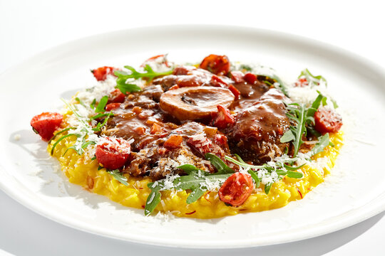 Traditional Italian dish - osso buco with risotto Milanese and cherry tomato and rucola. Ossobuco with saffron rice isolated on white background. Stewed meat on bone with yellow risotto.