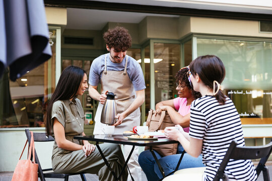 Barista pouring coffee for diverse women in summer cafe