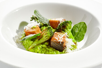 Gourmet food - green risotto with broccoli and salmon on white background. Italian lunch with risotto and sliced grilled salmon. Contemporary dish for restaurant menu. Hard shadow in sunshine day.