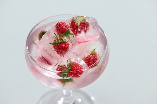 Glasses of drinks with fruit ice cubes on table against white