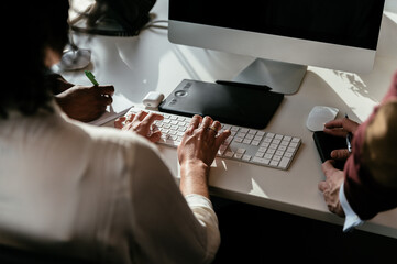 Crop colleagues working on computer at office
