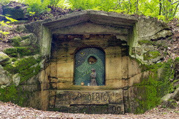 Chapel with a figure of the Virgin Mary holding Jesus Christ carved in stone wall in the forest, the 19th century, Czechia.
