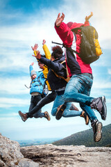Group of young happy friends having fun and jumping in top of the mountain - Hikers with backpacks celebrating success outdoor - People, success and sport concept.
