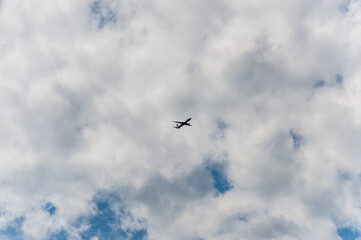 The plane is flying high in the sky under the clouds