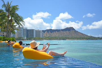 Tourists relaxing on rafts in oceanfront pool with Diamond Head and Pacific ocean views in Waikiki area of Honolulu on Oahu, Hawaii