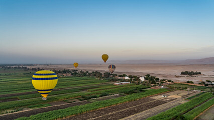 Bright balloons fly over the Nile Valley in Luxor. Cultivated green fields are visible below. Sand...